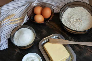 Baking ingredients for shortcrust pastry: butter, flour, eggs, sour cream, a towel on a wooden background. Flatley top view