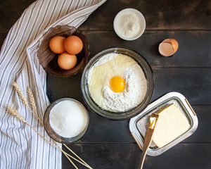 Baking ingredients for shortcrust pastry: butter, flour, eggs, sour cream, a towel on a wooden background. Flatley top view