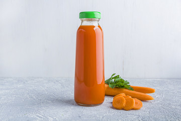 Nutritious detox carrot juice in glass bottle. Alkaline diet concept. Organic vegetarian drink and fresh carrots on gray background. Healthy eating. Close, copy space for text