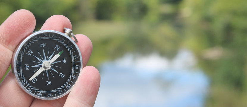 classic navigation compass in hand in summer against river as symbol of tourism with compass, travel with compass and outdoor activities with compass