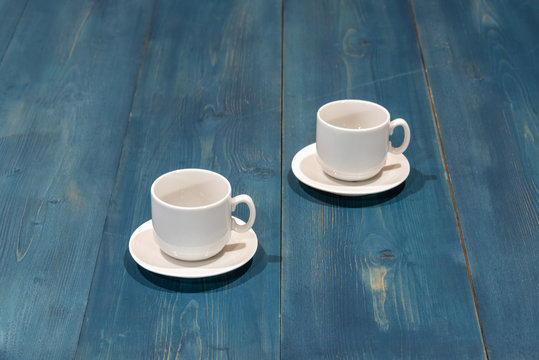 Two empty coffee cups on a blue wooden desk.