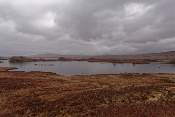 A bleak Loch Ba on Rannoch Moor on a wet day in April, with small Islands and large Boulders scattered across the Loch waters.