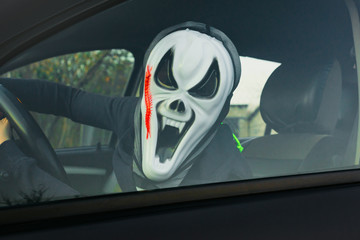Halloween. Man in a terrible mask in a car in the driver's seat harvests pumpkins and scares.