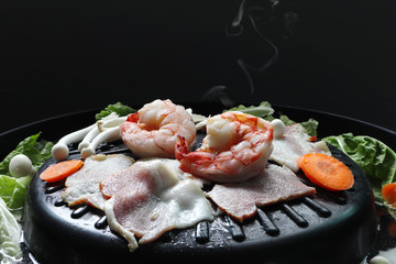 shrimps , bacon , prawns , carrot and mushroom are on the electric barbecue grill hot pot on the black table in the shabu sukiyaki restaurent
