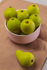 On a kitchen towel brown wild pears in a plate. One pear lies near a plate