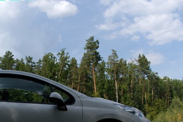 Fototapeta na wymiar side view of front of white passenger car on blurred background of green forest and blue sky