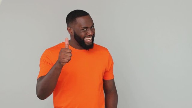Young bearded african american guy 20s in orange basic t-shirt look at camera with charming smile pointing fingers on you applause cheering clapping hands isolated on grey color gray background studio