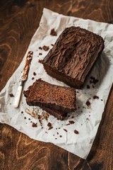 Sliced chocolate loaf cake and a knife on baking paper on dark wooden background