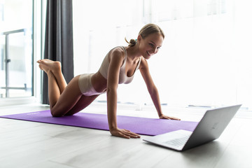Young sports woman doing workout on the floor at home and watching fitness videos in a laptop.