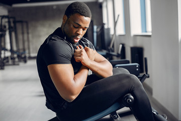 Sports man in the gym. A black man performs exercises. Guy in a black t-shirt