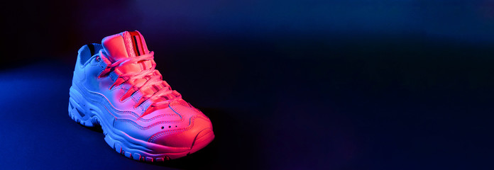 White sneaker on black background in the neon red and blue light. Banner.