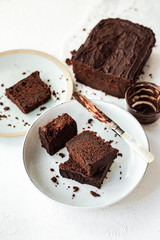 Fototapeta na wymiar Sliced chocolate loaf cake served on two plates, a knife covered with chocolate, high key, white background