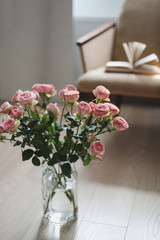 Cozy room with flowers in a vase, armchair and a book. Festive interior decoration.  Living room decorated with flowers