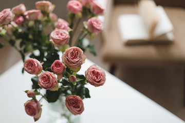 Cozy room with flowers in a vase, armchair and a book. Festive interior decoration.  Living room decorated with flowers