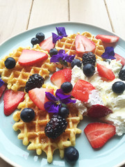 Top view of waffles, berries, whipped cream and edible flowers on a plate.