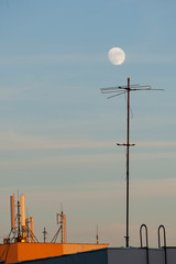 Antennas on top of buildings at sunset with the full moon on top. - 372892892