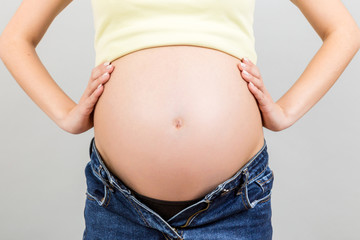 Cropped image of pregnant woman in unzipped jeans showing her naked belly at colorful background with copy space. Baby expecting concept