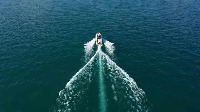 Large white boat with an awning fast movement on dark blue water to meet the sun at sunset, view from the top to the boat 4k video