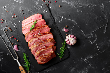 Medium rare Ribeye steak with spices and herbs on a black stone background. Top view, flat lay, copy space.