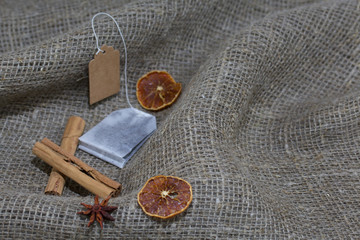 Tea bag on a coarse linen cloth. Nearby are cinnamon, dried orange slices and anise. Autumn still life.