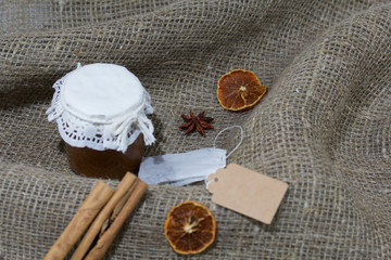 Jar of jam and tea bag on a rough linen cloth. Nearby are cinnamon, dried orange slices and anise....