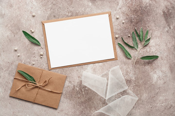 Beautiful female wedding background with accessories. Blank card mockup, silk ribbon, olive branch and leaves, craft envelope, pearls. Invitation template. Top view, flat lay.
