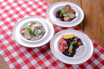 Grilled meat pieces with sauce, pasta with pesto, black pasta with salmon fish and lemon.