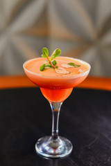 Tropical mixed drink with mint leaves served in tall glass on rustic wooden table over blurred restaurant background.