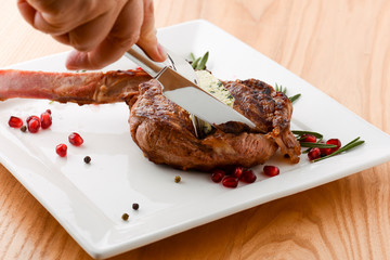 Rack of lamb served with pomegranate seeds and sauce on white plate. Close-up hands cutting rack of...