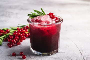 Fresh ice cold fruit cocktail in glass, refreshing summer red currant berry drink with rosemary leaf on stone concrete background, angle view