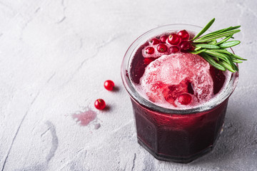 Fresh ice cold fruit cocktail in glass, refreshing summer red currant berry drink with rosemary leaf on stone concrete background, angle view copy space