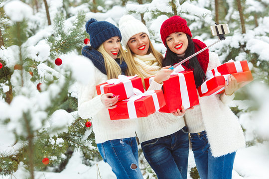 Group of young girls makin selfie with christmas presents outdoors. Cheerful friends making a picture on the mobile camera