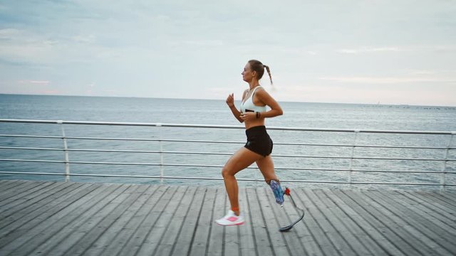 Motivated disabled girl running at seaside, side view, slow motion