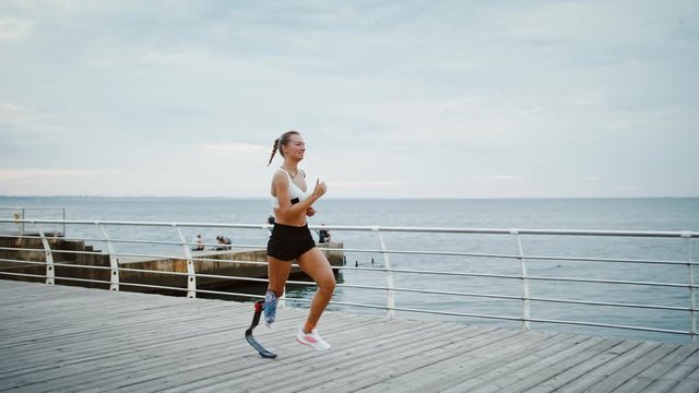 Young disabled female runner training at seaside, slow motion