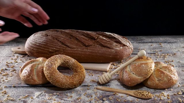 Baker put fresh organic rye bread on cutting board on the table with bun and bagels and flour decoration 