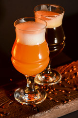 Two tulip beer glasses on dark wooden table over black background. Dark and light beer, stout beer, wheat beer.