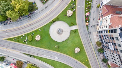 Aerial view of roundabout. There is a grass field at the center. People are standing for Friday Pray on grass.