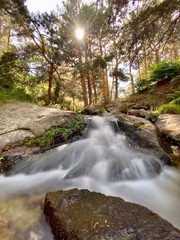 Obraz premium Cascada con un pequeño lago en verano en la sierra con los rayos del sol