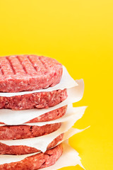 Raw beef patties in a stack isolated on a yellow background. Hamburger beef patties close-up