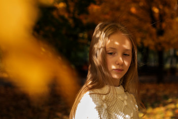 beautiful blonde teen girl walking in an autumn Park with maple trees
