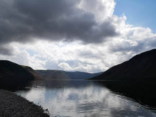 lake sorrounded by hills reflected in the water, grey clouds on the sky