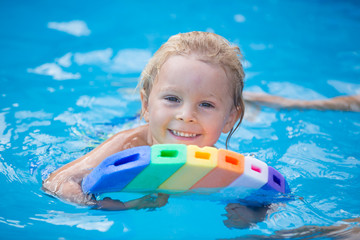 Cute toddler boy, swimming in pool with board