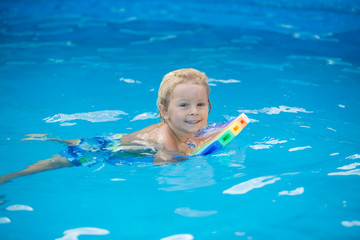 Fototapeta na wymiar Cute toddler boy, swimming in pool with board