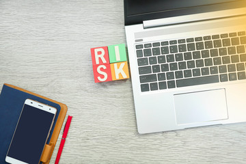 Risk concept with letter RISK on colorful cubes with a laptop, smartphone on the notebook, and a pen on the wooden table