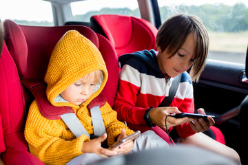 Three children, boys, traveling in car in carseat and playing on mobiles