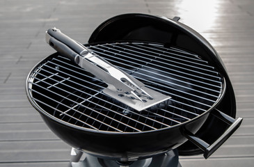 Black barbecue grill isolated with instruments on the terrace with composite