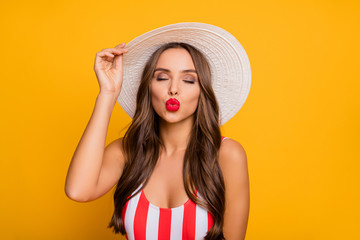 Photo of adorable gentle lady perfect long hairstyle sexy smooth bronze body send boyfriend air kisses red lips wear sun hat striped swim bodysuit isolated bright yellow color background