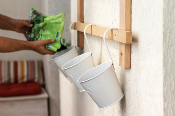 White metal pots for plants hanging on wooden shelf on wall. In the background, a man fills a pot with soil.