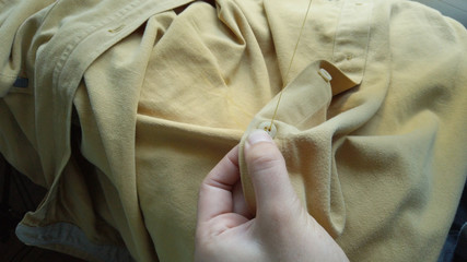 Close up woman's hands sewing a button to a yellow shirt. Female at work	
