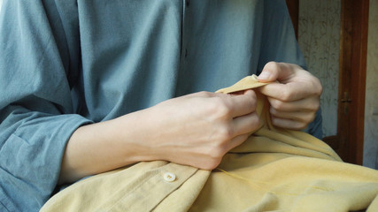 Close up woman's hands sewing a button to a yellow shirt. Female at work